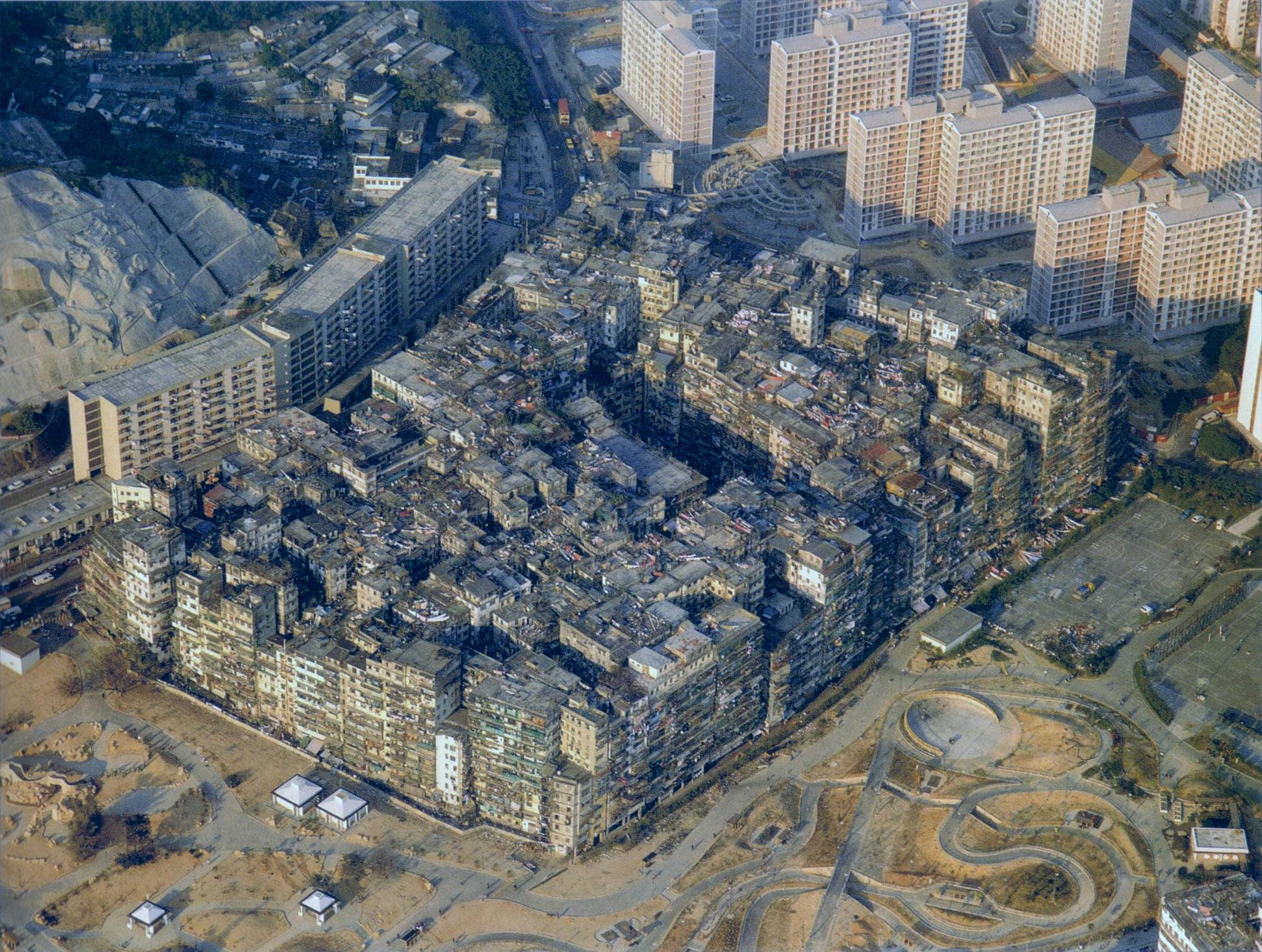 Image of Kowloon Walled City in 1989 priar to it's demolishon in 1993-1994. There is a gap in the center of the walled city where the yamen building is located. The buildings are at their max height and packed so tightly there is no space between them.